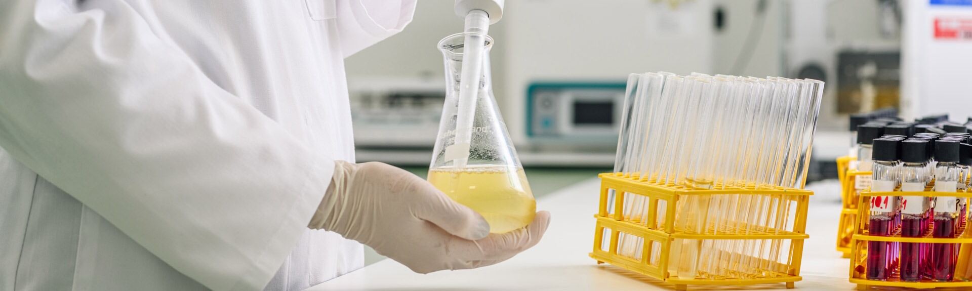 A gloved hand holds a flask with yellow liquid in a laboratory setting