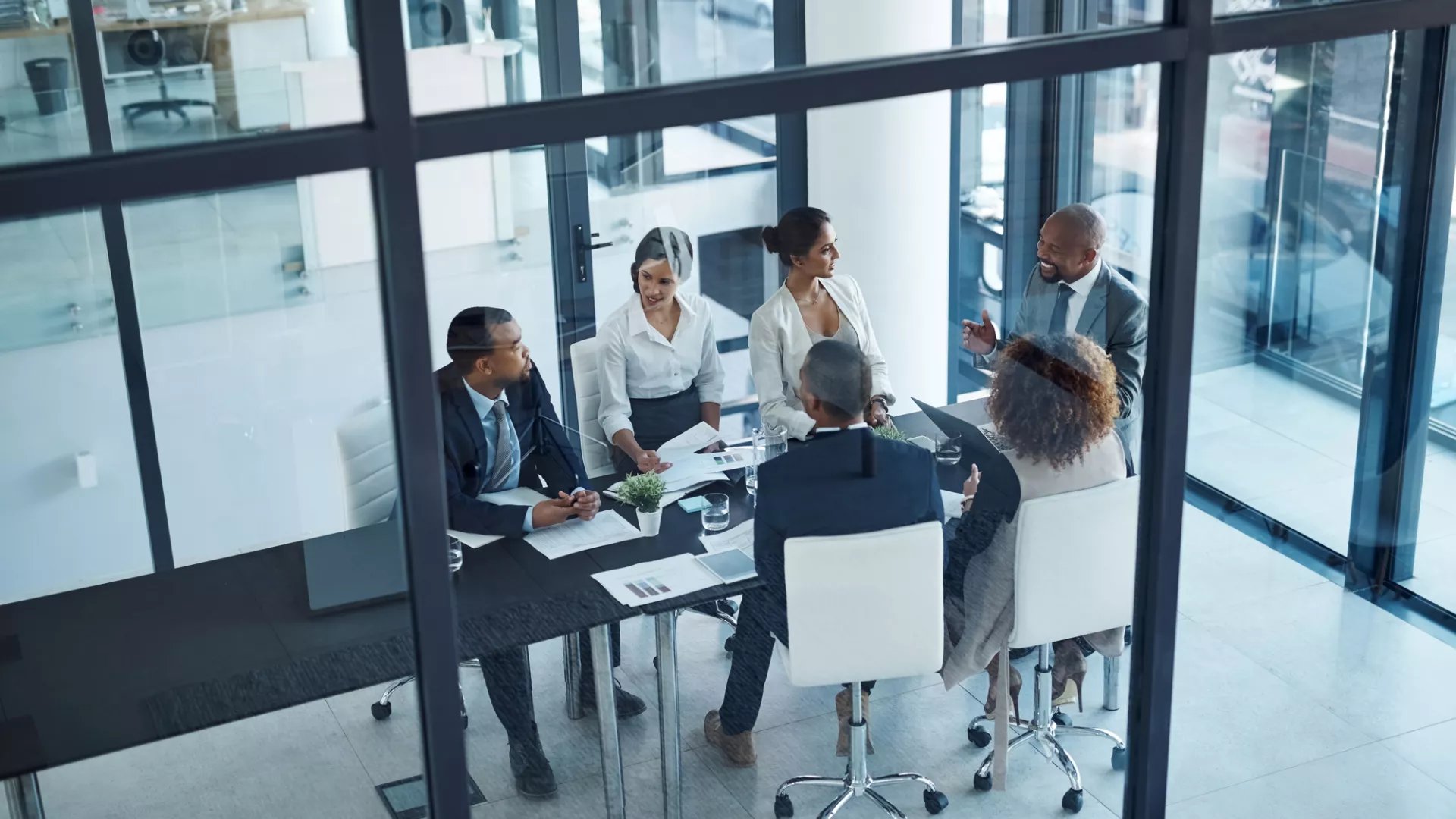 A group of professionals engages in a meeting around a table in a modern office setting.